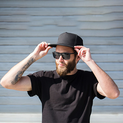 A man with beard and sunglasses holding his hat