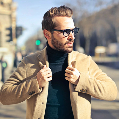 A man in glasses and a coat is standing on the street.