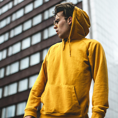 A man in yellow hoodie standing next to a building.